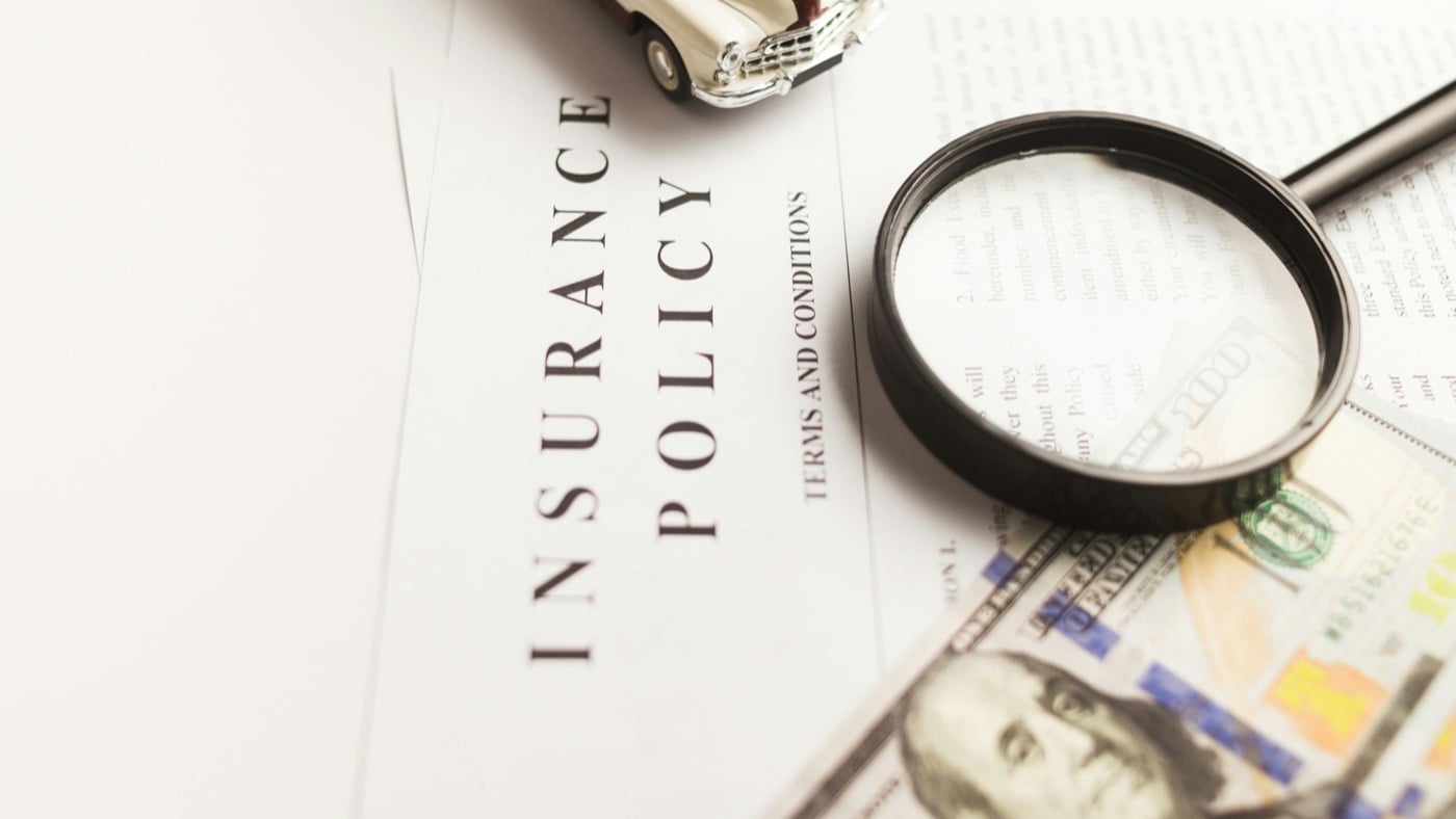 An insurance policy document beside a magnifying glass and banknotes