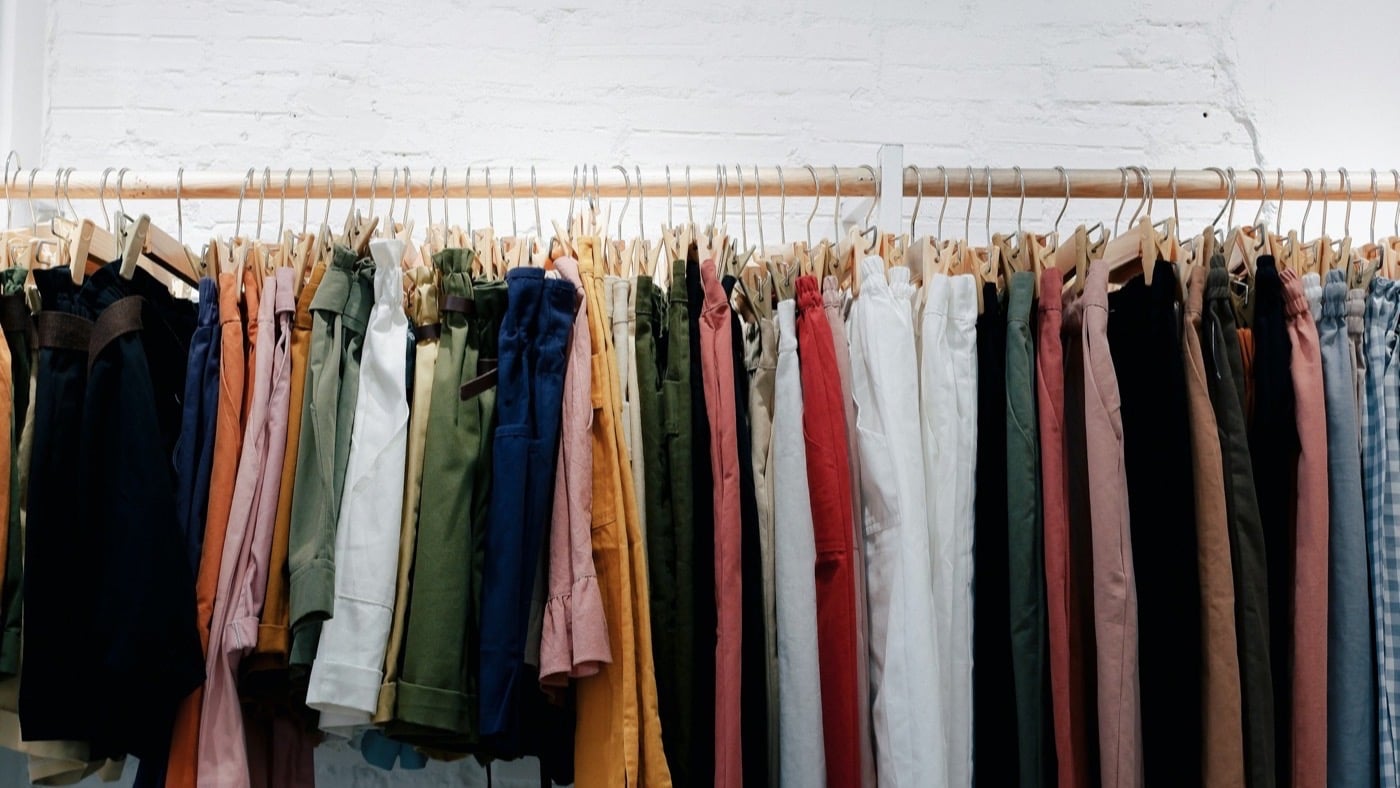 A long rail of clothes on wooden hangers against a white brick wall