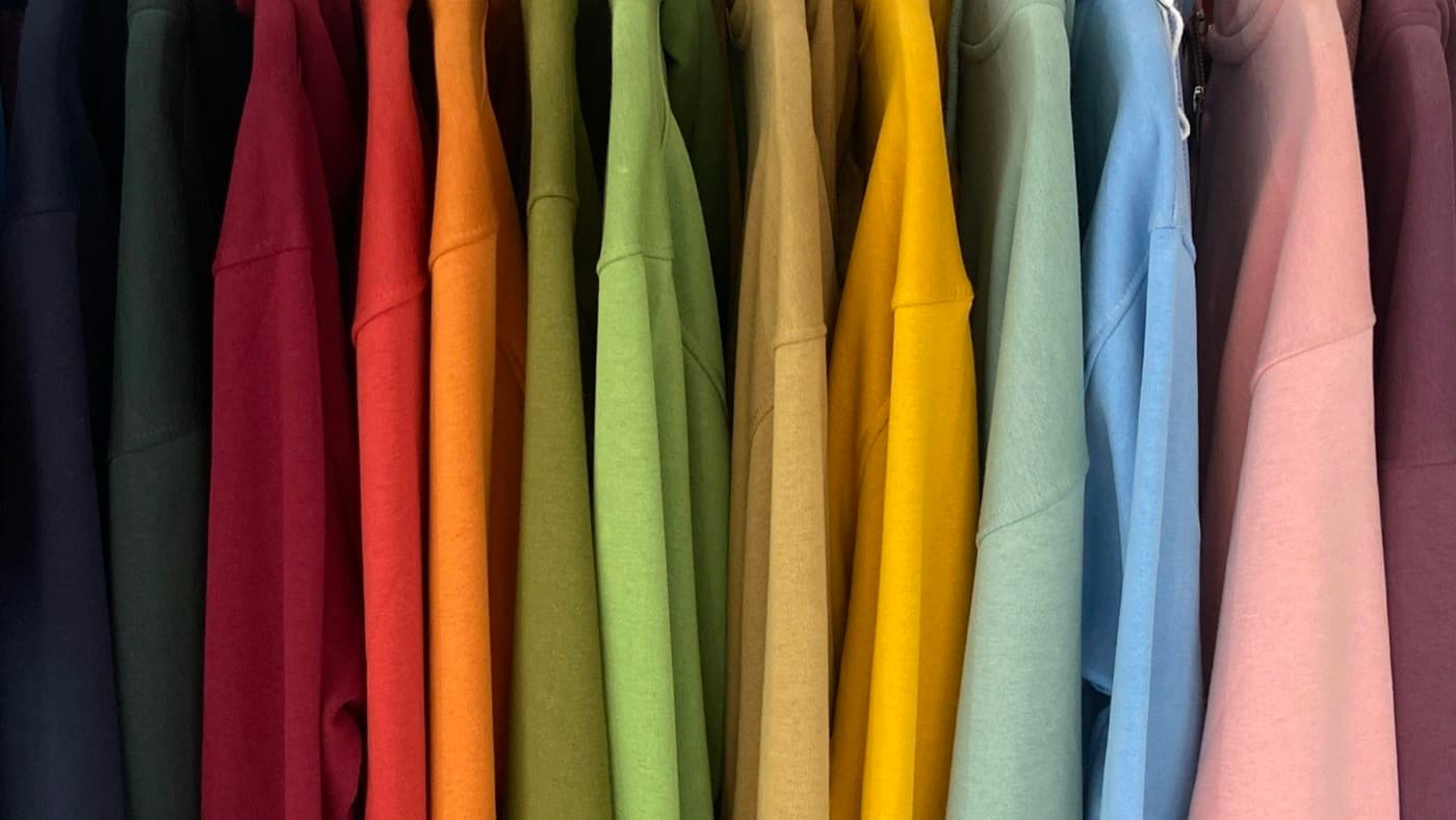 A rack of shirts in a range of colors hanging on wooden hangers