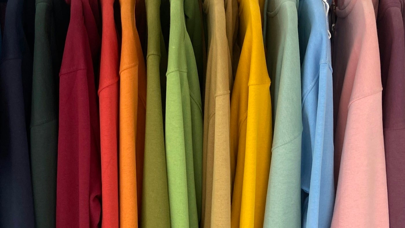 A rack of shirts in a range of colors hanging on wooden hangers