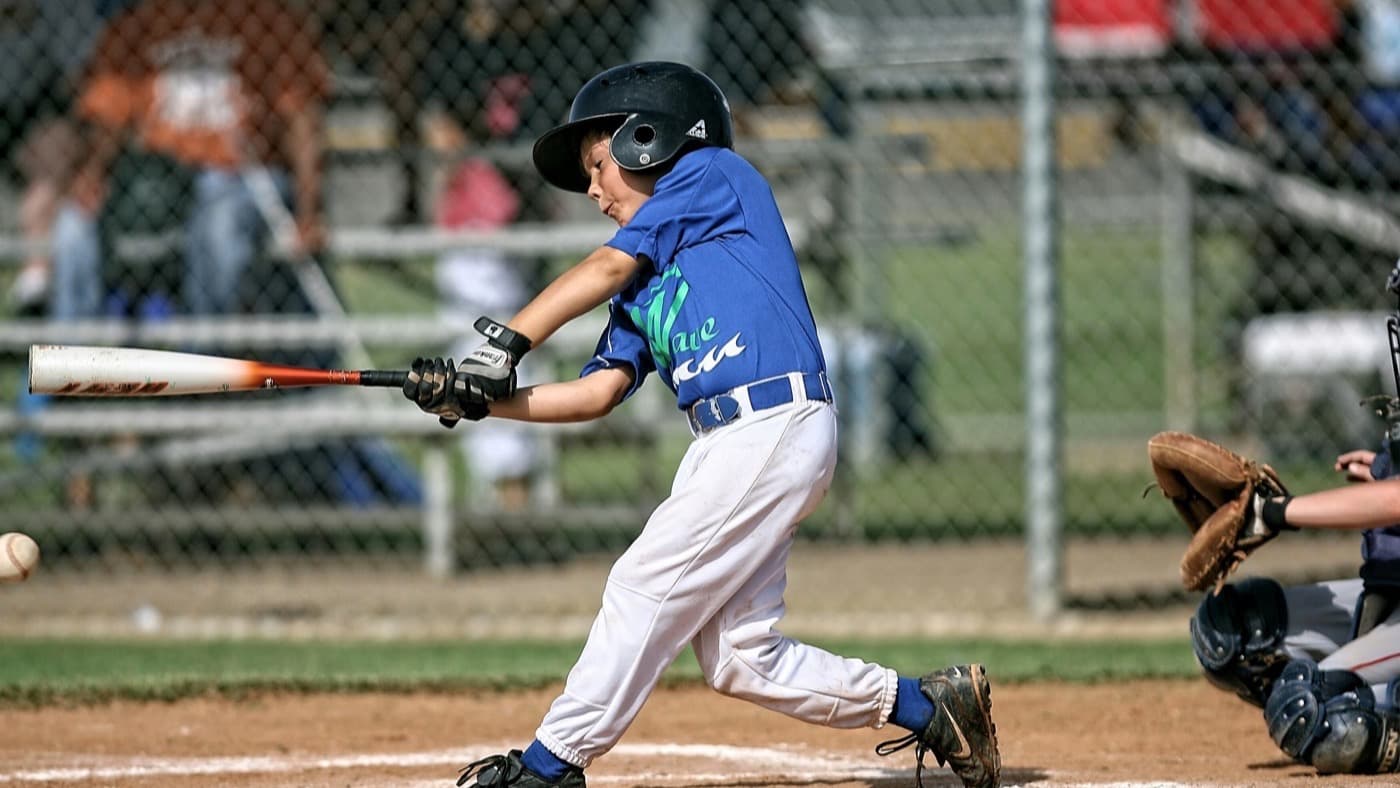 A young baseball player in a team jersey swinging at a pitch
