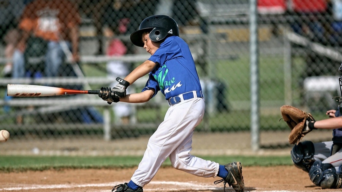 A young baseball player in a team jersey swinging at a pitch